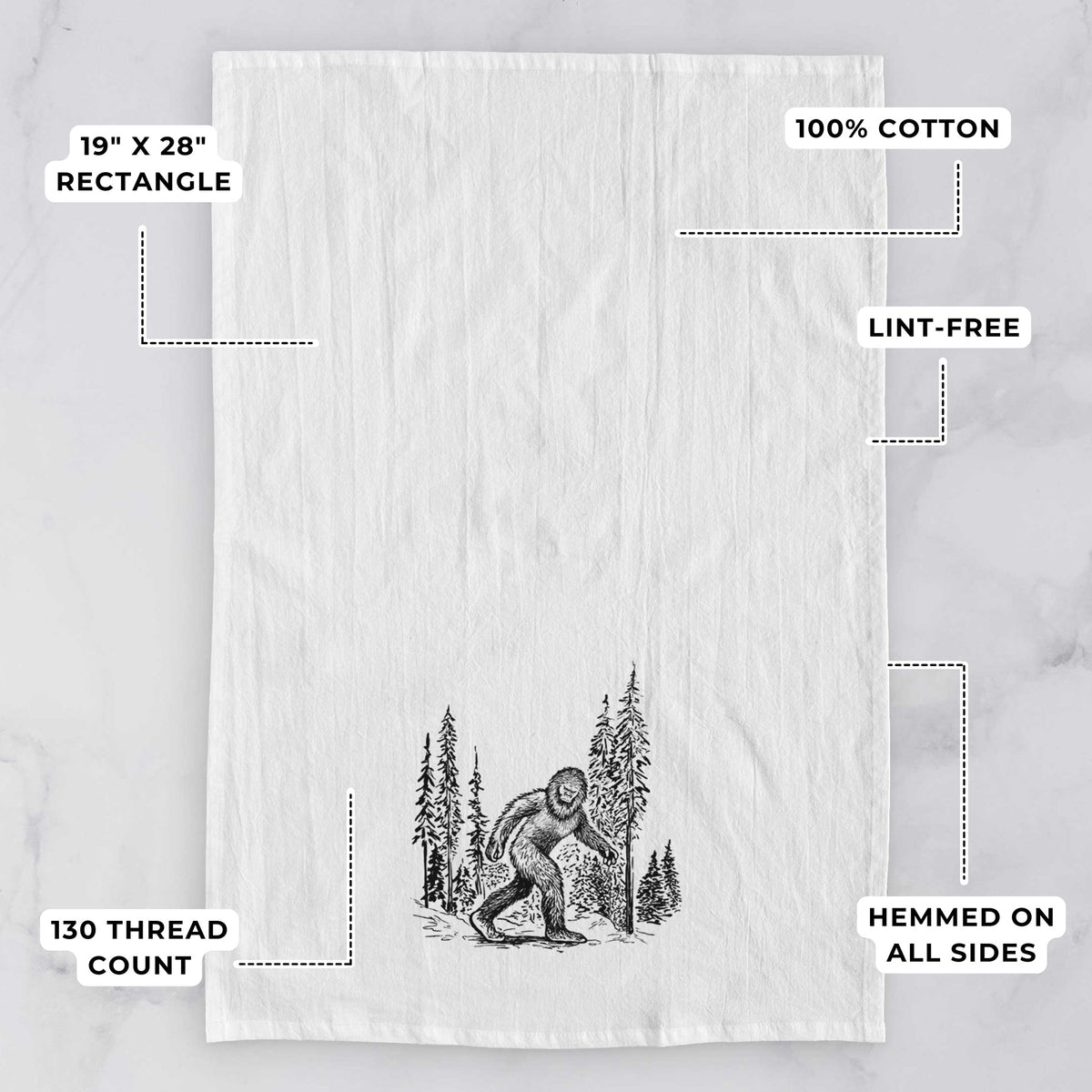 White tea towel printed with a black ink illustration of Bigfoot walking through a pine forest, with feature labels: 19 by 28 inch rectangle, 100% cotton, lint-free, 130 thread count, hemmed on all sides.
