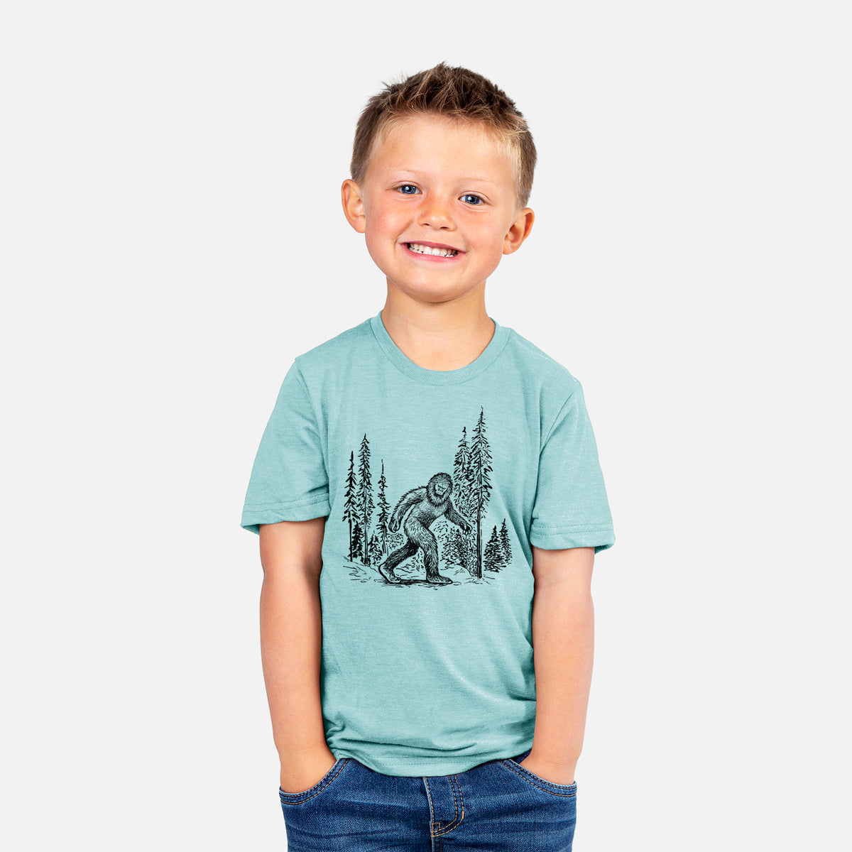 Smiling boy wearing a youth t-shirt printed with a black ink illustration of Bigfoot walking through a pine forest.
