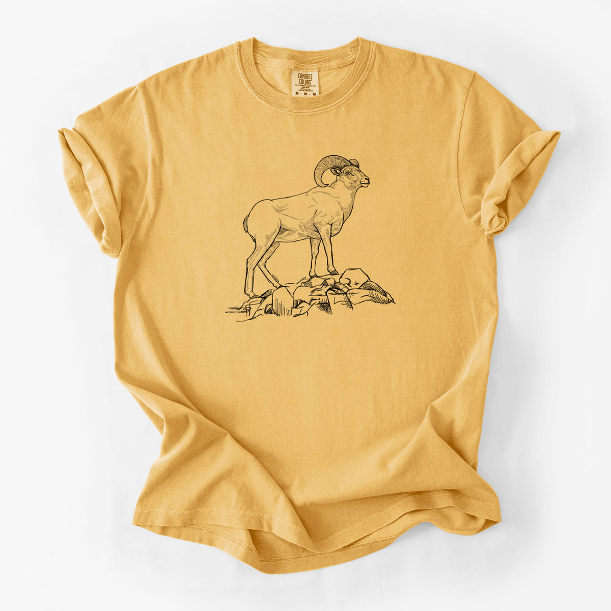 Golden wheat yellow Comfort Colors t-shirt laid flat, printed with a black ink illustration of a bighorn ram with curled horns standing on rocks.