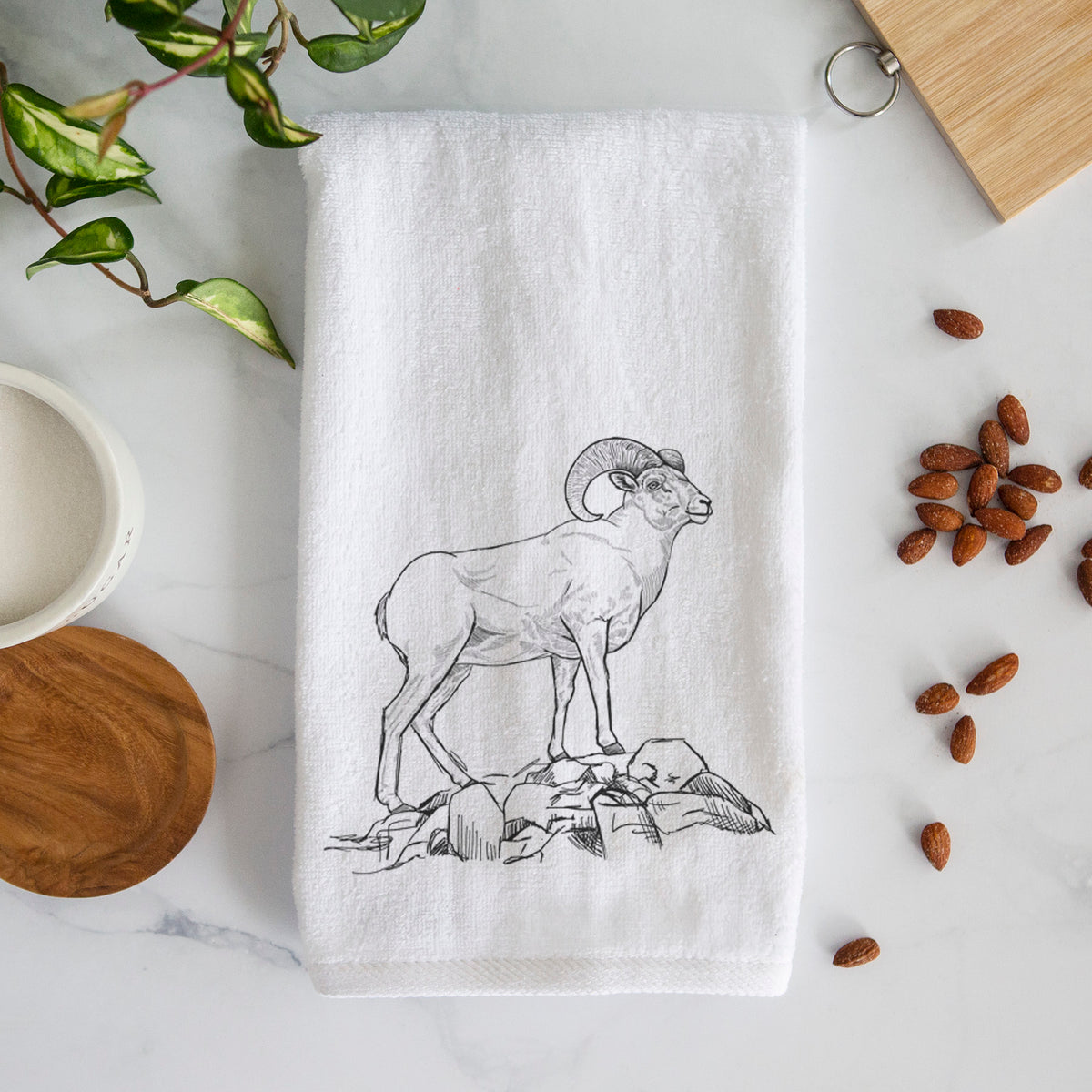 White hand towel printed with a black ink illustration of a bighorn ram with curled horns standing on rocks.
