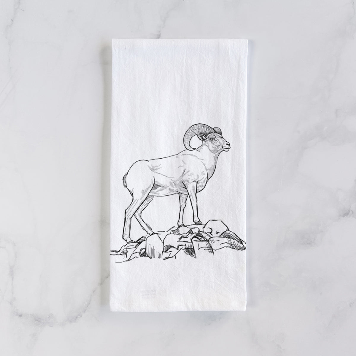 White cotton tea towel laid flat on marble, printed with a black ink illustration of a bighorn ram with curled horns standing on rocks.
