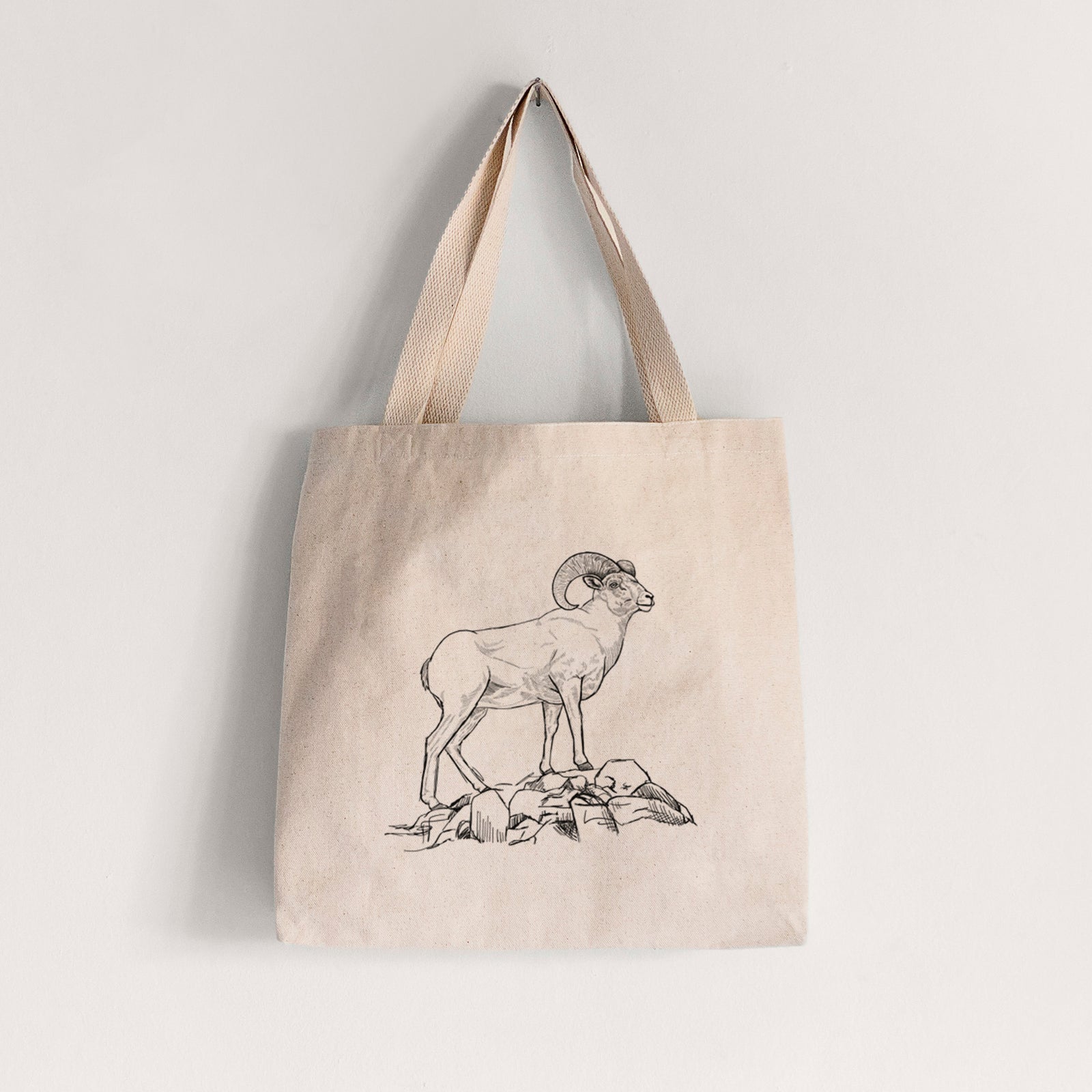 Natural canvas tote bag printed with a black ink illustration of a bighorn ram with curled horns standing on rocks.