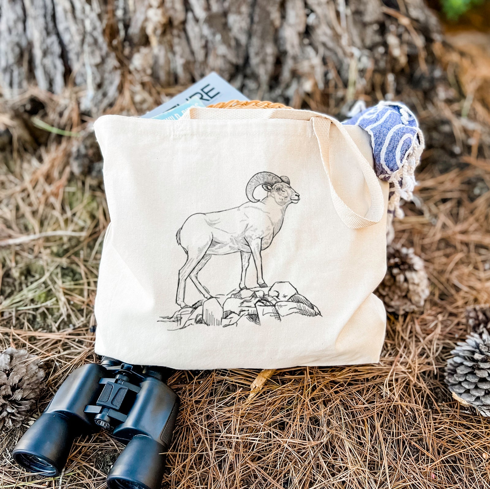 Natural canvas tote bag printed with a black ink illustration of a bighorn ram with curled horns standing on rocks.