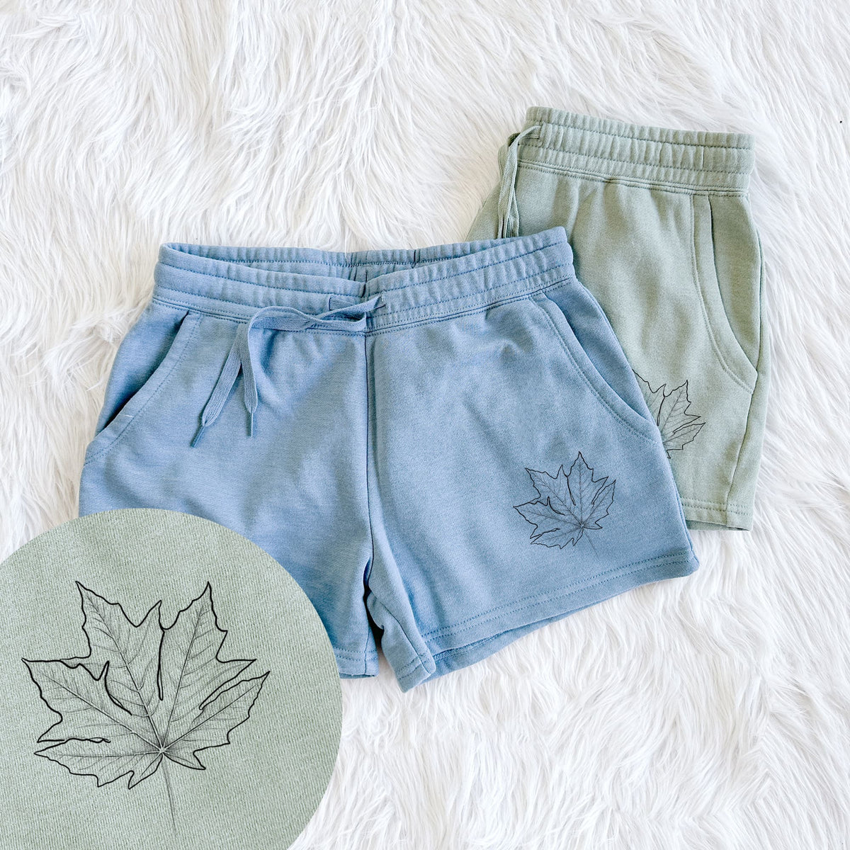 Two pairs of Cali Wave shorts in different colors printed with a black ink line drawing of a bigleaf maple leaf, with a close-up of the print.
