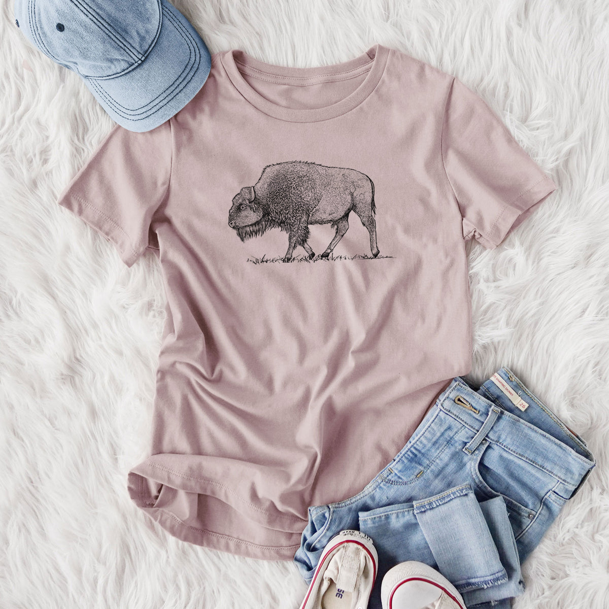 Women's relaxed fit cotton t-shirt printed with a detailed black ink illustration of an American bison walking through grass, styled flat on a white faux fur rug with jeans.
