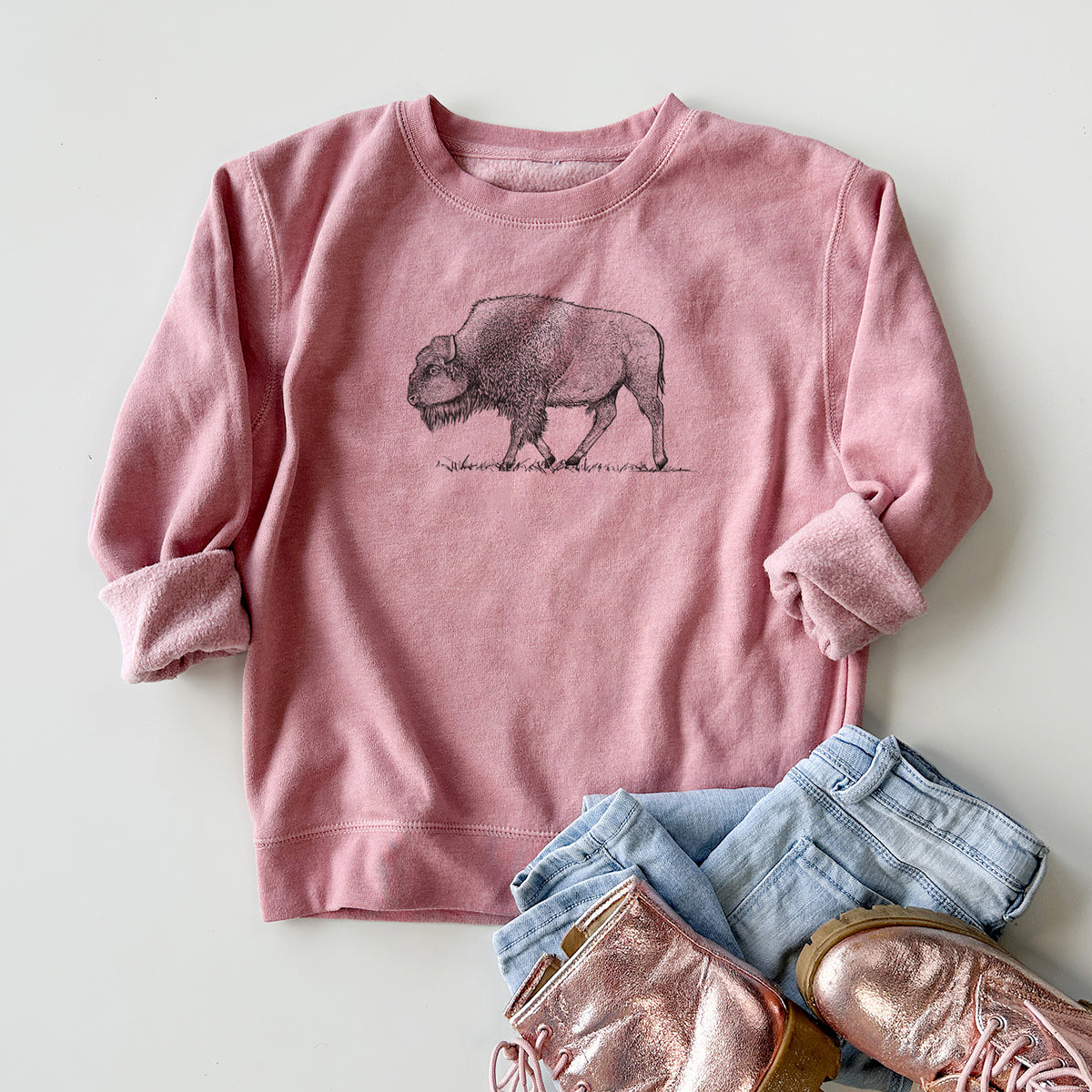 Youth crewneck sweatshirt printed with a detailed black ink illustration of an American bison walking through grass, styled flat with jeans and boots.