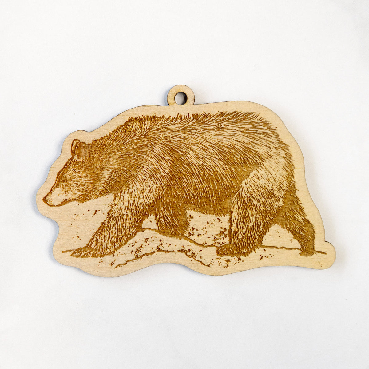Wooden ornament featuring a detailed engraving of a black bear walking across rocky ground, on a marble surface.