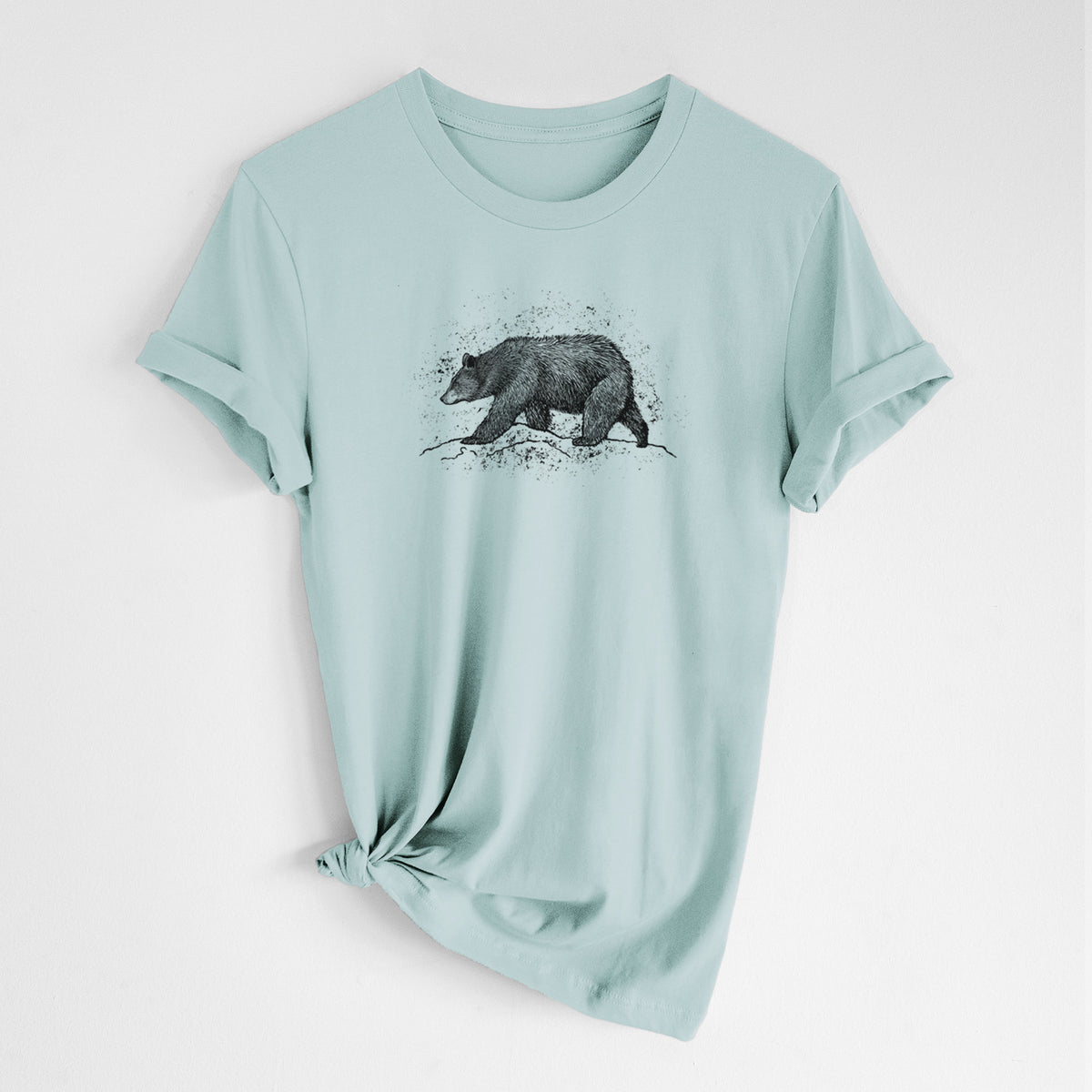 Dusty blue lightweight cotton t-shirt laid flat with the sleeves rolled, printed with a detailed black ink sketch of a black bear walking across rocky ground.