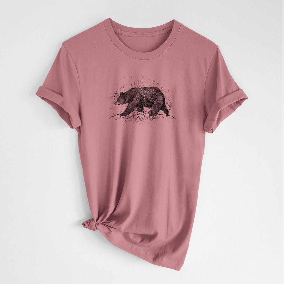 Mauve pink lightweight cotton t-shirt laid flat with the sleeves rolled, printed with a detailed black ink sketch of a black bear walking across rocky ground.