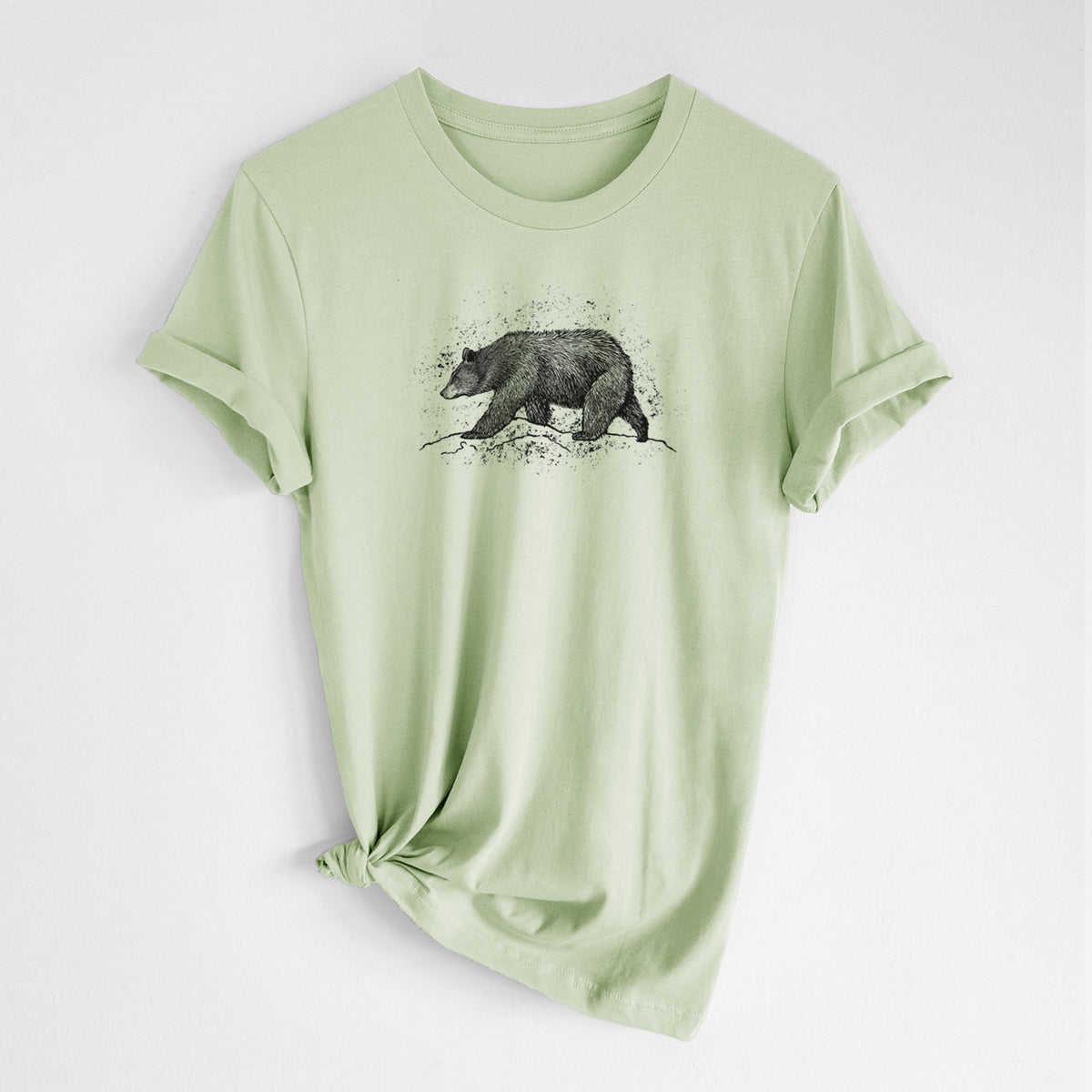 Spring green lightweight cotton t-shirt laid flat with the sleeves rolled, printed with a detailed black ink sketch of a black bear walking across rocky ground.