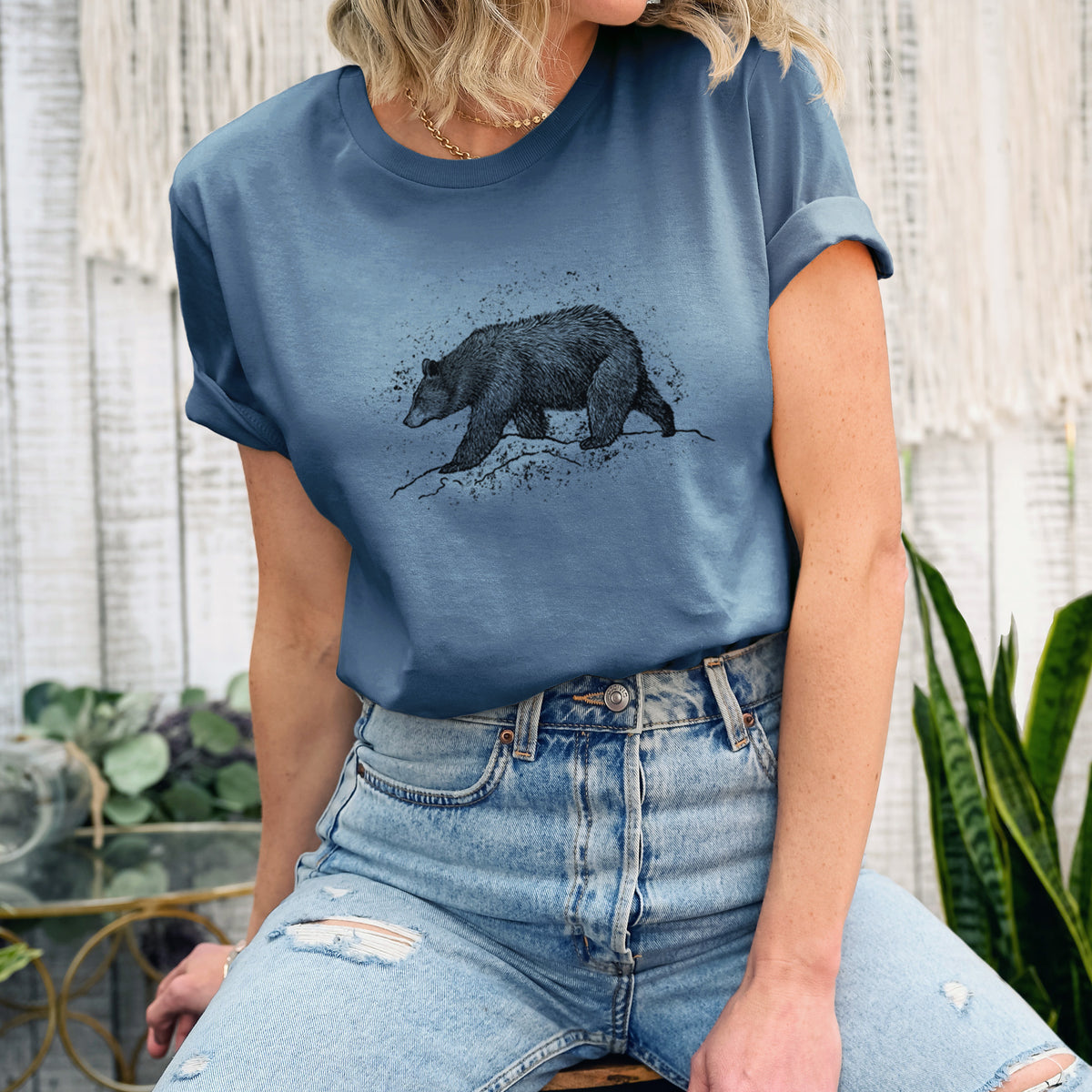 Woman wearing a steel blue lightweight cotton t-shirt printed with a detailed black ink sketch of a black bear walking across rocky ground.