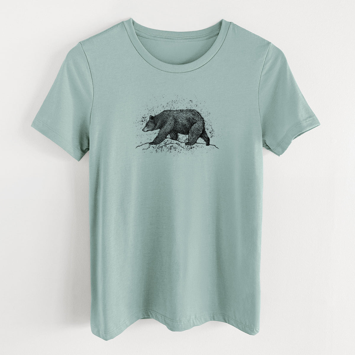 Dusty blue women's relaxed fit cotton t-shirt laid flat, printed with a detailed black ink sketch of a black bear walking across rocky ground.