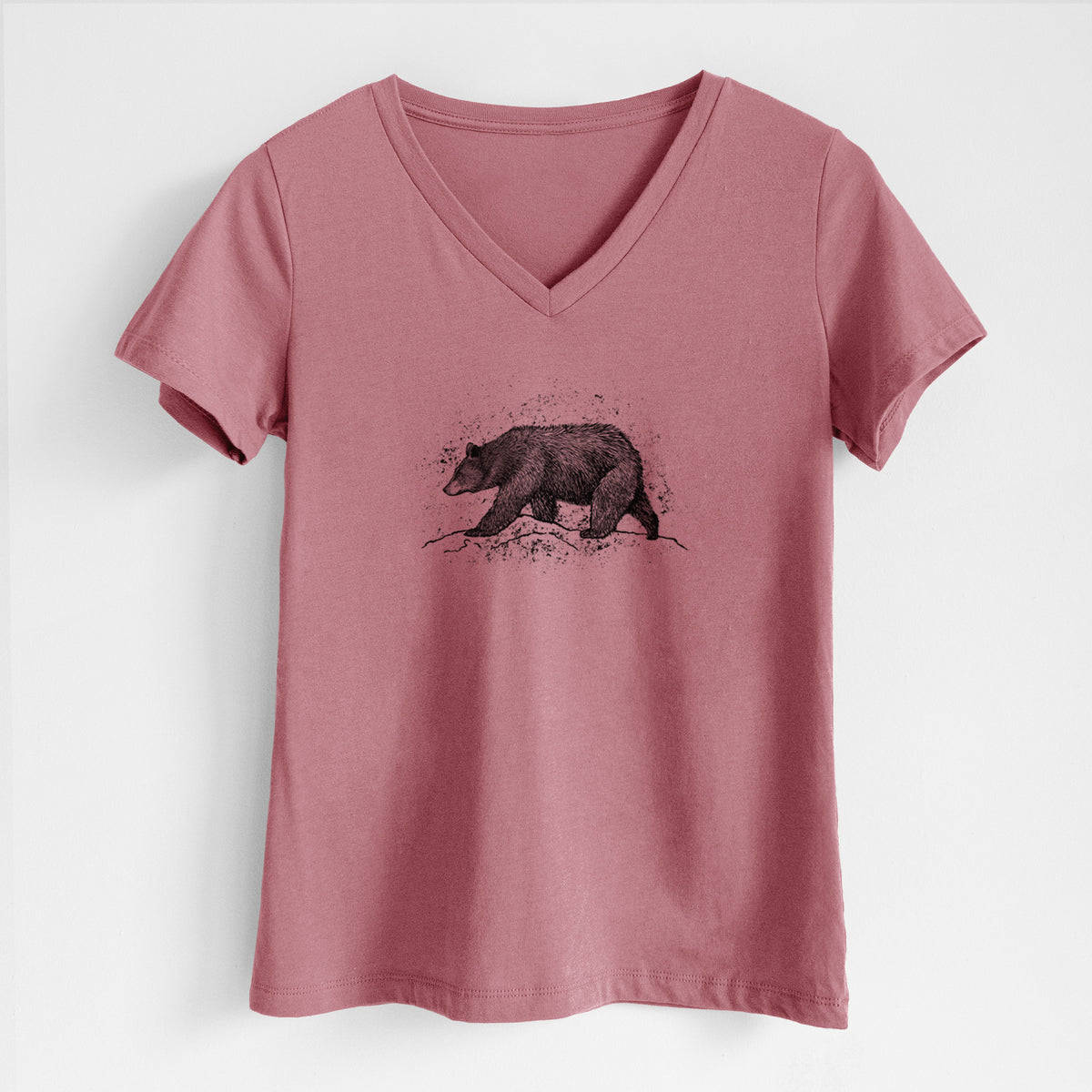 Mauve pink women's relaxed fit cotton V-neck t-shirt laid flat, printed with a detailed black ink sketch of a black bear walking across rocky ground.