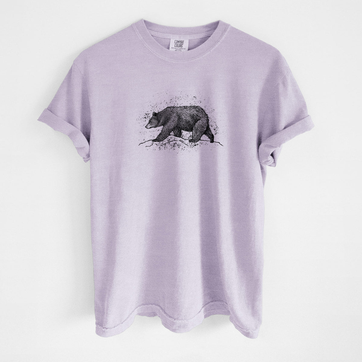 Orchid purple Comfort Colors t-shirt laid flat, printed with a detailed black ink sketch of a black bear walking across rocky ground.