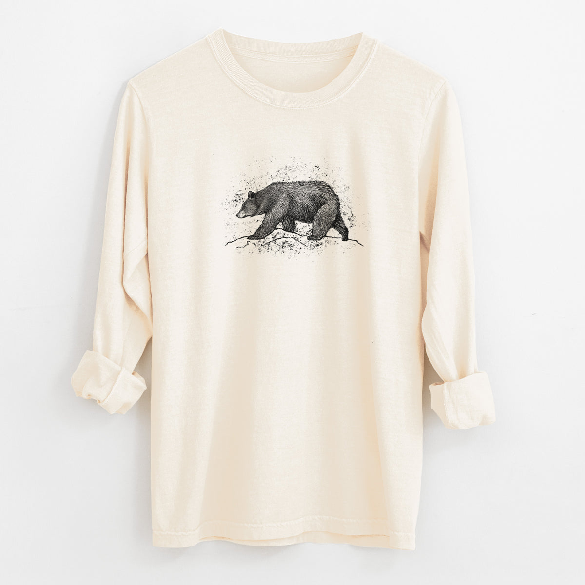 Ivory Comfort Colors long sleeve shirt laid flat with the cuffs rolled, printed with a detailed black ink sketch of a black bear walking across rocky ground.