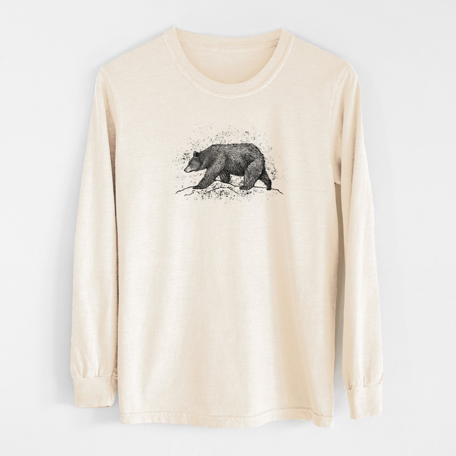 Ivory Comfort Colors long sleeve shirt laid flat, printed with a detailed black ink sketch of a black bear walking across rocky ground.