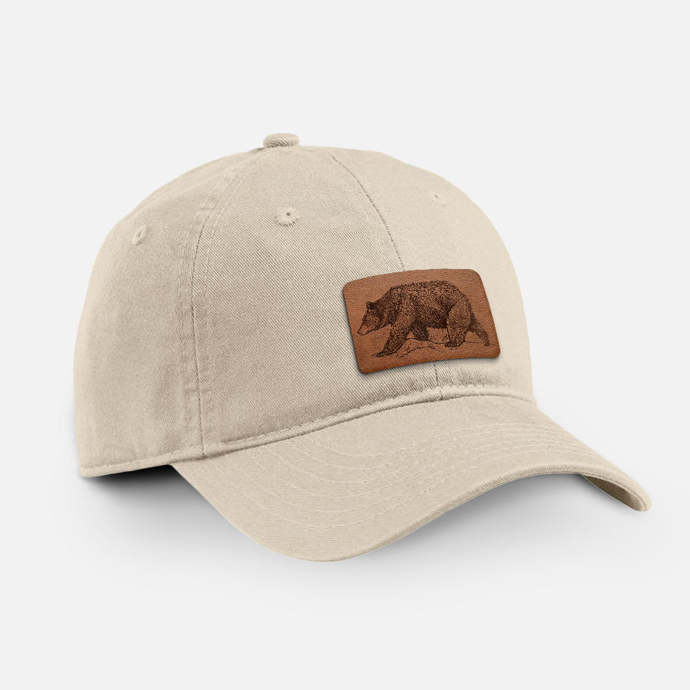 Stone cotton baseball hat with a detailed black ink sketch of a black bear walking across rocky ground on the front.