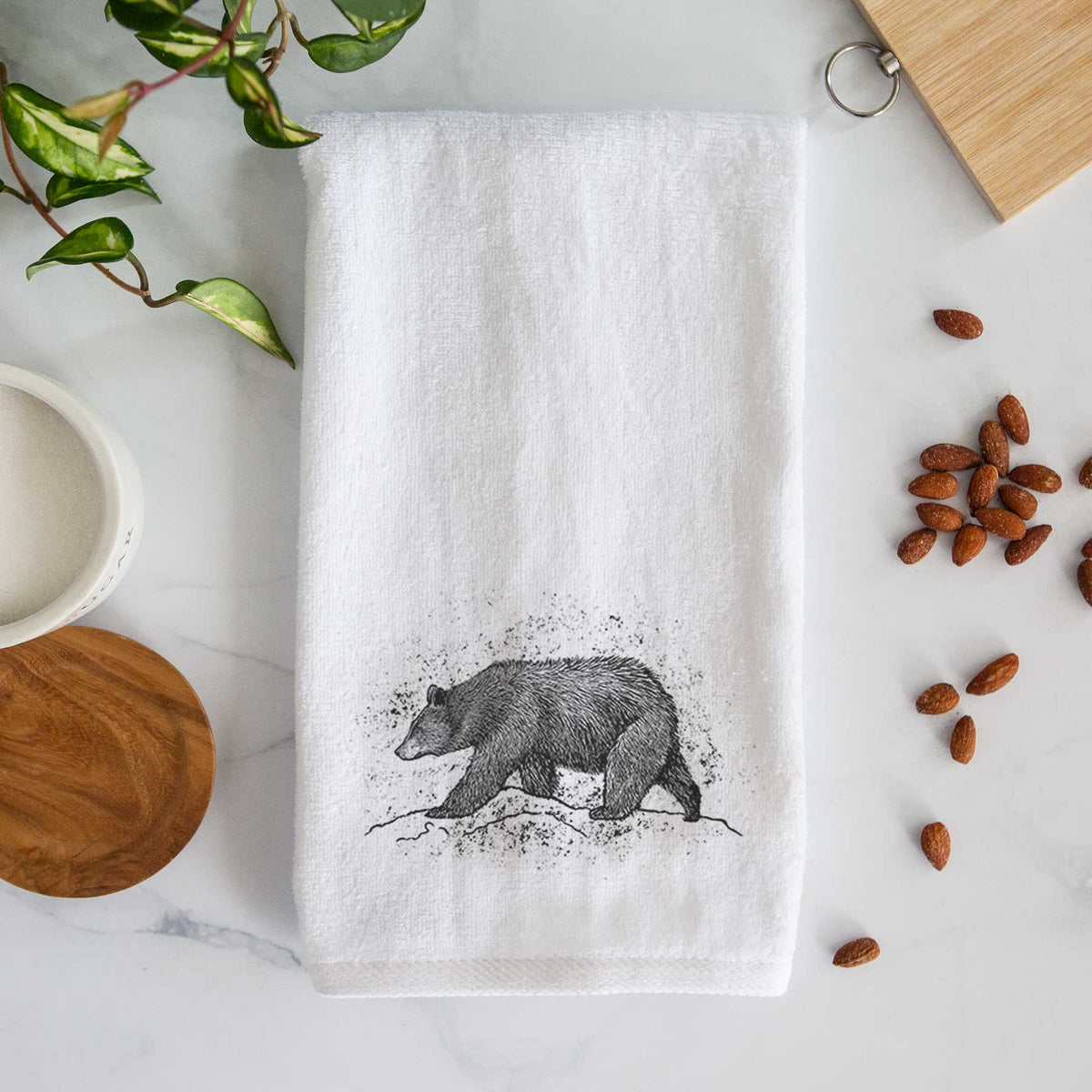 White hand towel printed with a detailed black ink sketch of a black bear walking across rocky ground.