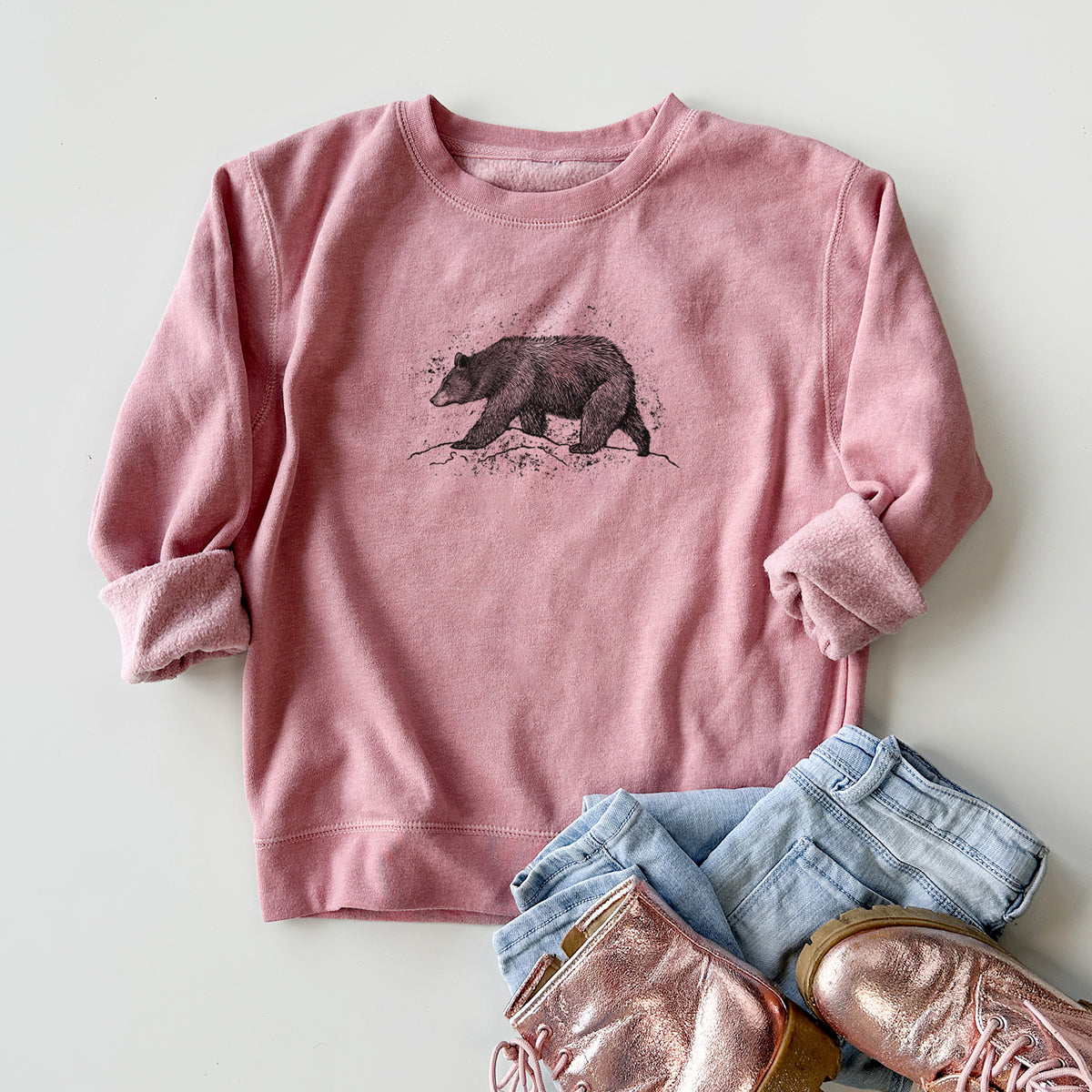 Youth crewneck sweatshirt printed with a detailed black ink sketch of a black bear walking across rocky ground, styled flat with jeans and boots.