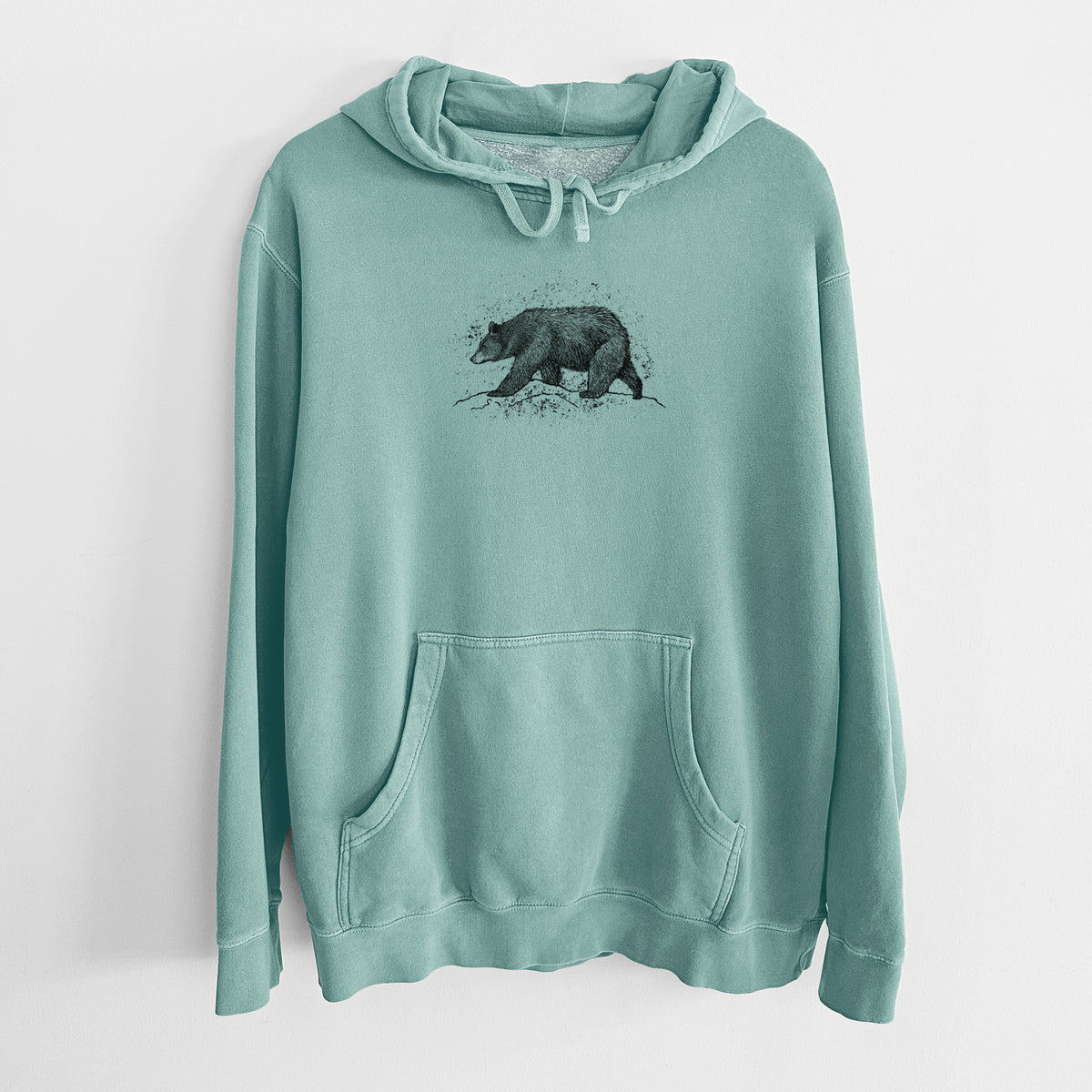 Mint green pigment dyed hoodie laid flat, printed with a detailed black ink sketch of a black bear walking across rocky ground.