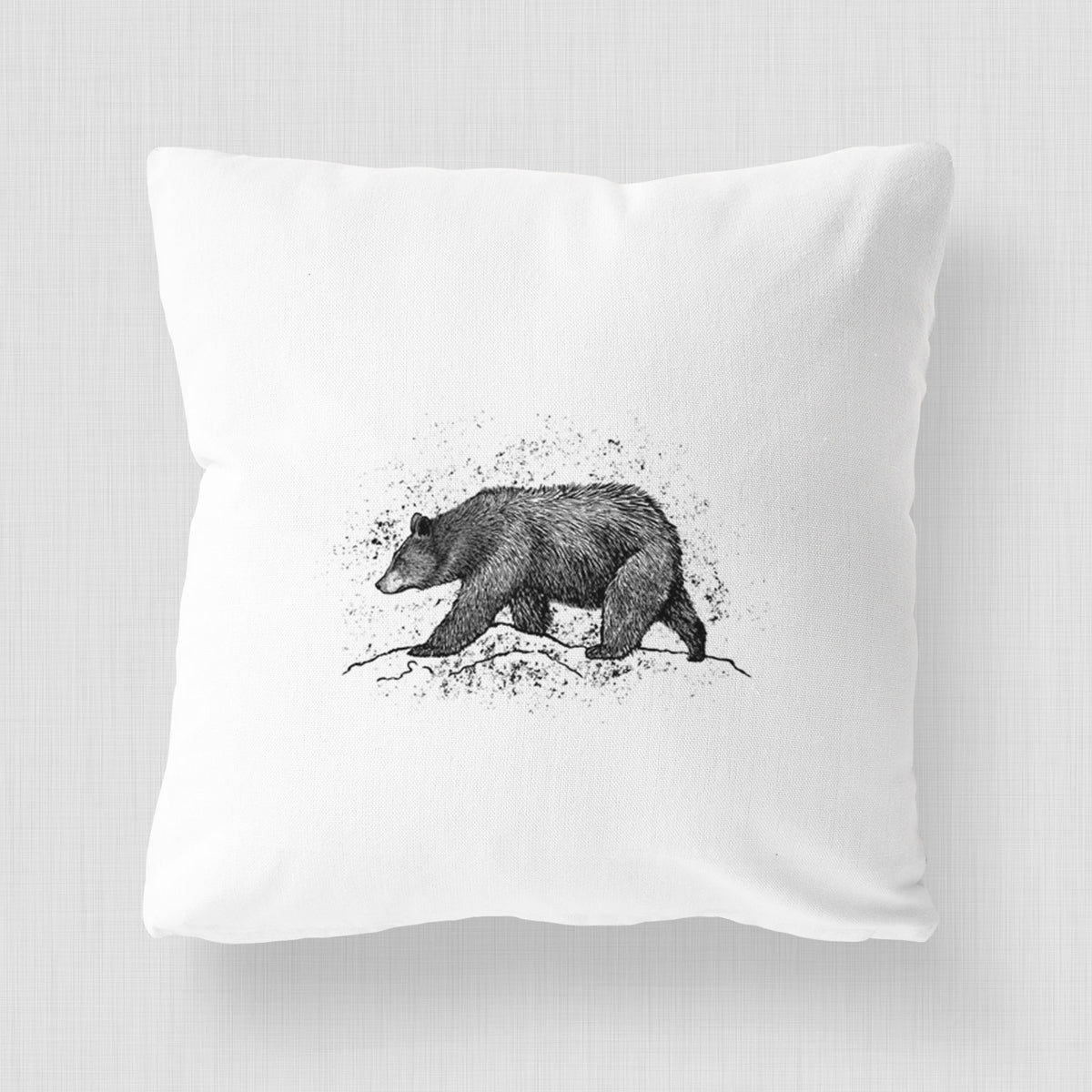 White pillow cover printed with a detailed black ink sketch of a black bear walking across rocky ground.