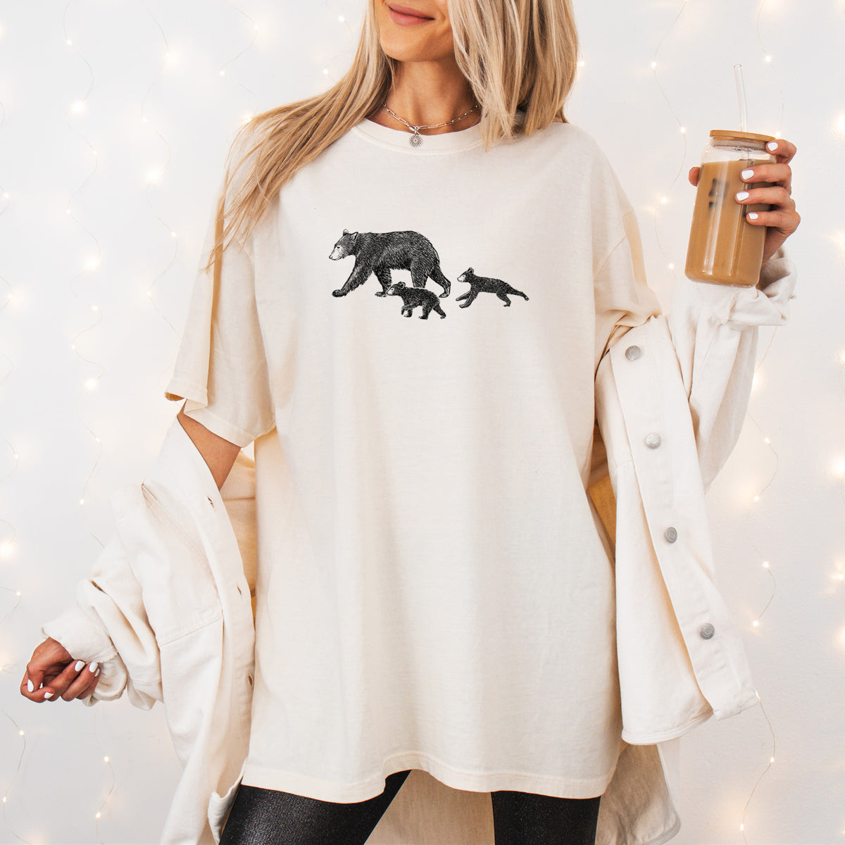 Woman wearing a Comfort Colors t-shirt printed with a black ink illustration of a mother black bear walking with two cubs, outdoors.