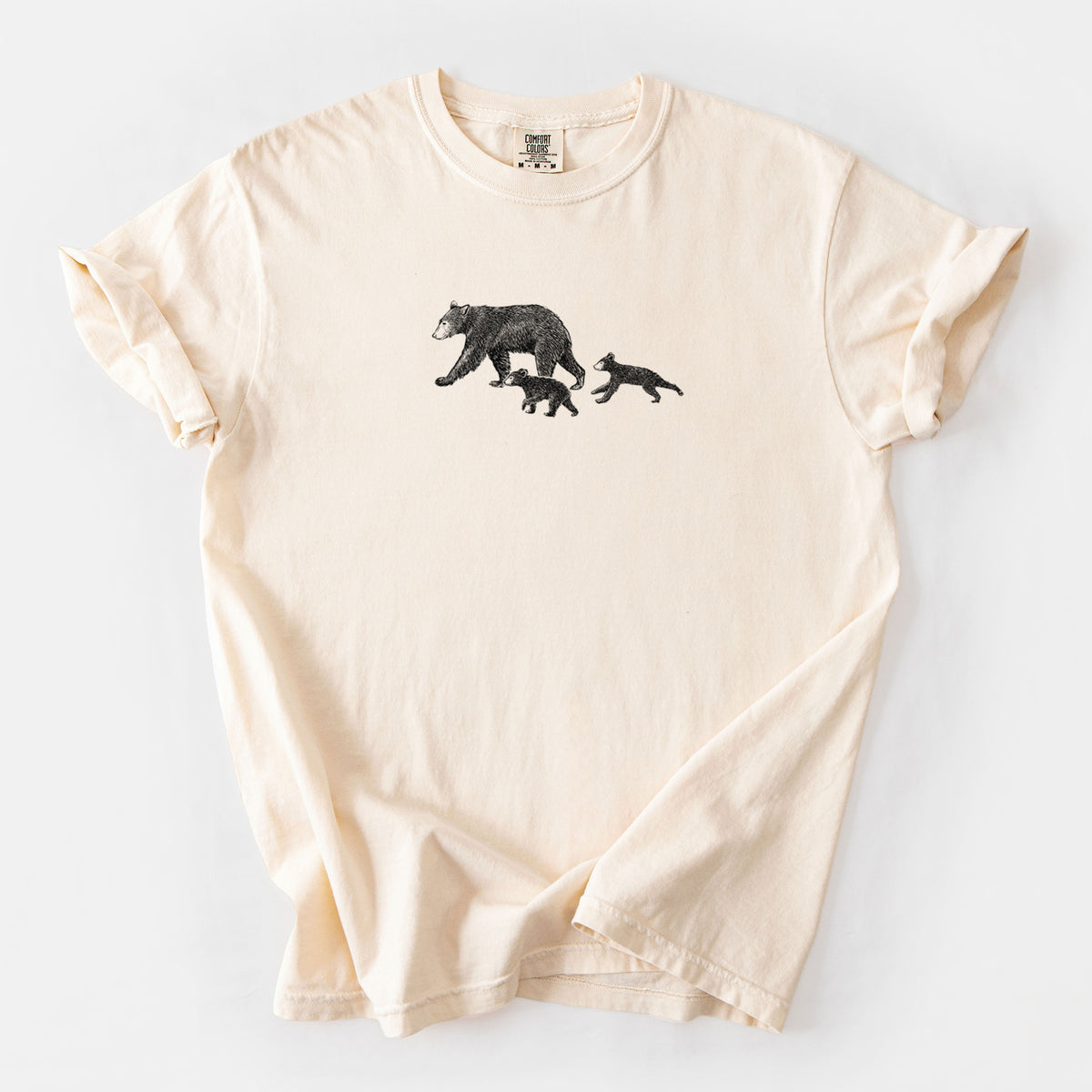 Ivory Comfort Colors t-shirt laid flat, printed with a black ink illustration of a mother black bear walking with two cubs.