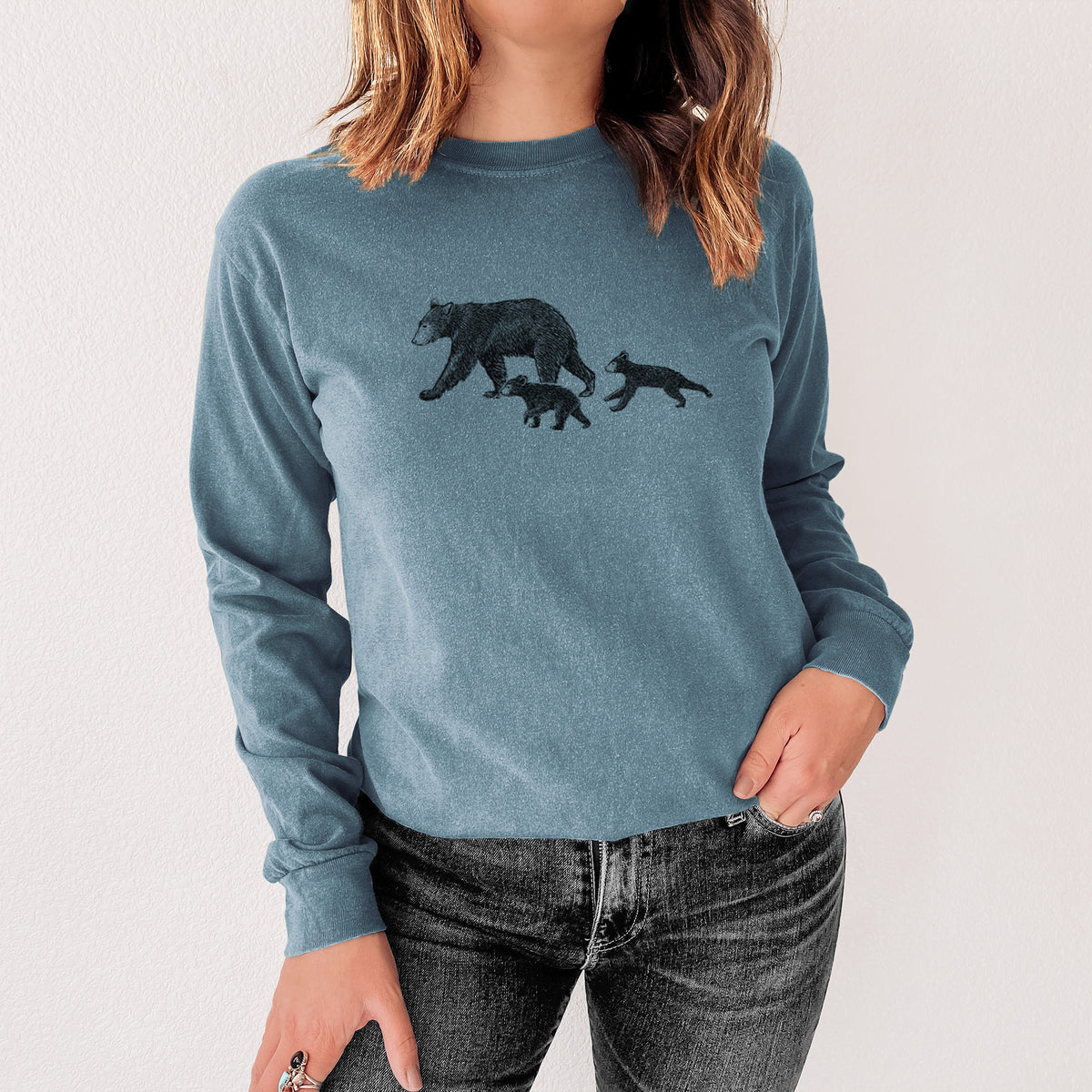 Steel blue Comfort Colors long sleeve shirt printed with a black ink illustration of a mother black bear walking with two cubs, shown in a lifestyle photo.