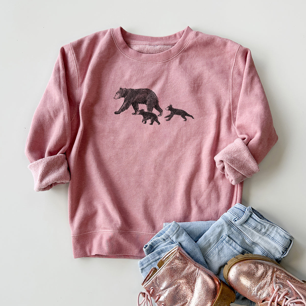 Youth crewneck sweatshirt printed with a black ink illustration of a mother black bear walking with two cubs, styled flat with jeans and boots.