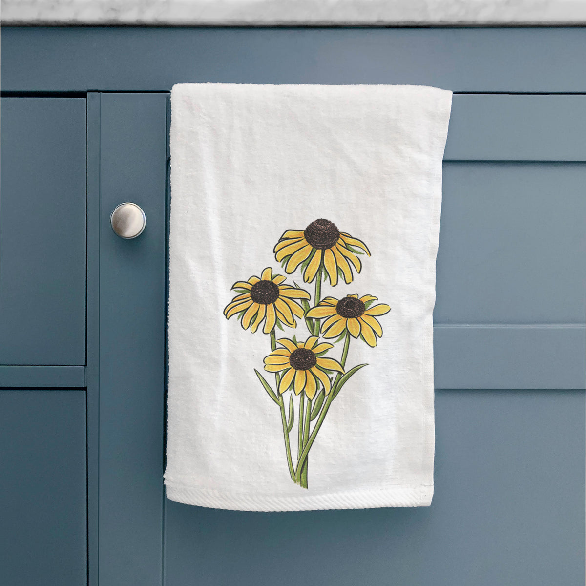 White hand towel printed with a full-color bouquet of yellow black-eyed Susan flowers, hanging on a cabinet door.