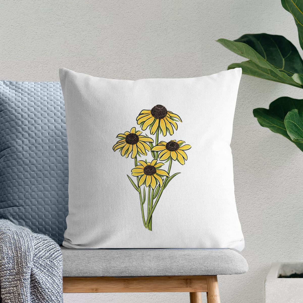 White pillow cover printed with a full-color bouquet of yellow black-eyed Susan flowers, on a bench beside plants.