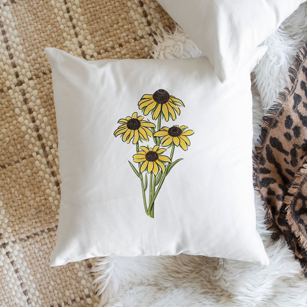 White pillow cover printed with a full-color bouquet of yellow black-eyed Susan flowers, on a woven chair.