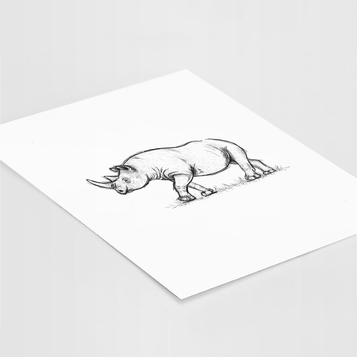 Art print of a black ink illustration of a black rhinoceros walking, lying at an angle on a white surface.