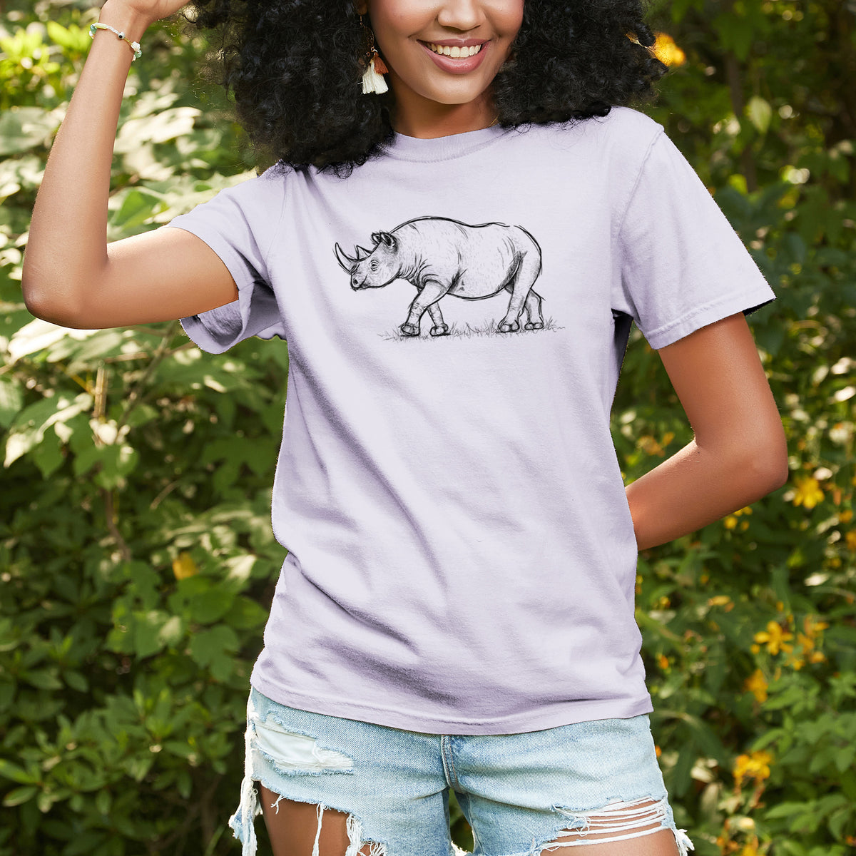 Woman wearing a Comfort Colors t-shirt printed with a black ink illustration of a black rhinoceros walking, outdoors.