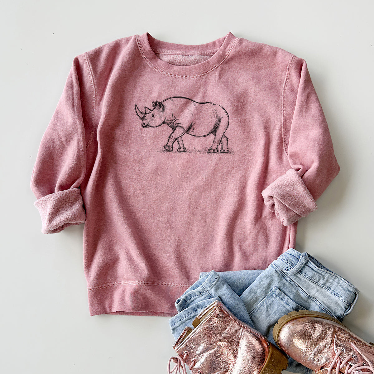 Youth crewneck sweatshirt printed with a black ink illustration of a black rhinoceros walking, styled flat with jeans and boots.