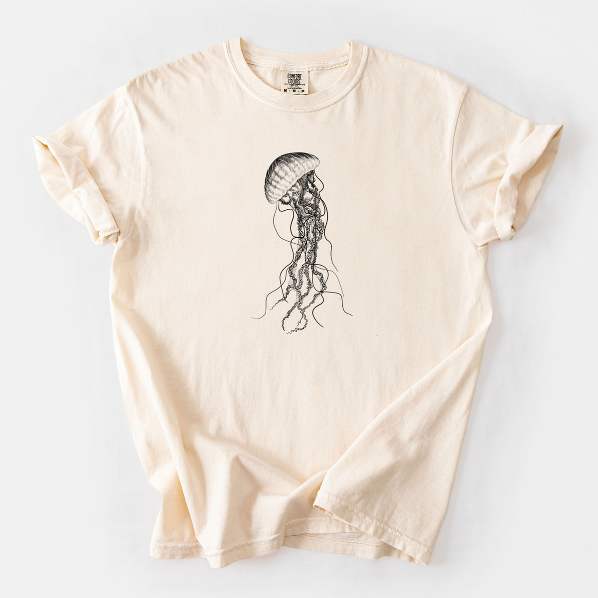 Ivory Comfort Colors t-shirt laid flat, printed with a black ink illustration of a black sea nettle jellyfish with long trailing tentacles.