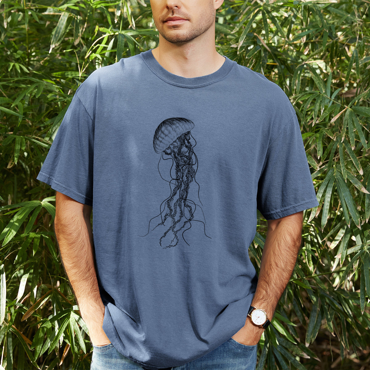 Man wearing a Comfort Colors t-shirt printed with a black ink illustration of a black sea nettle jellyfish with long trailing tentacles, outdoors.