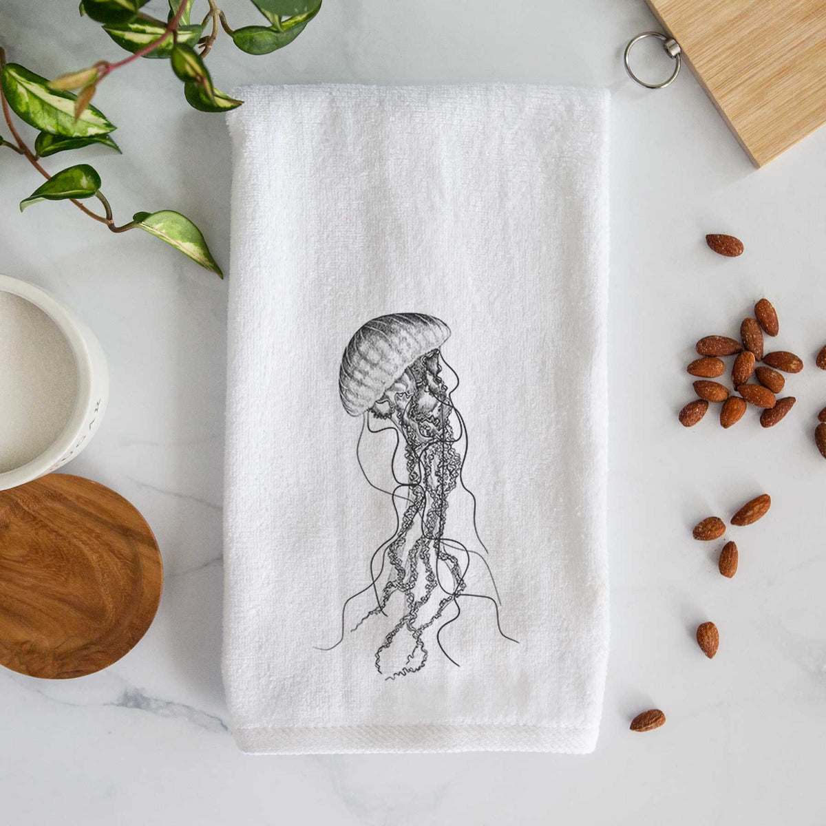 White hand towel printed with a black ink illustration of a black sea nettle jellyfish with long trailing tentacles.