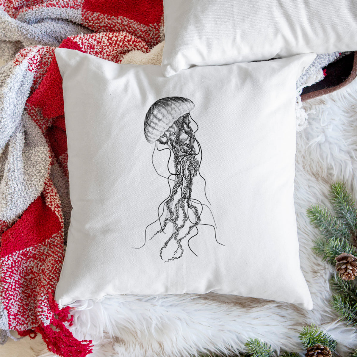 White pillow cover printed with a black ink illustration of a black sea nettle jellyfish with long trailing tentacles, on a woven chair.