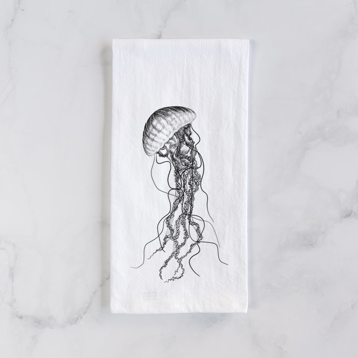 White cotton tea towel laid flat on marble, printed with a black ink illustration of a black sea nettle jellyfish with long trailing tentacles.