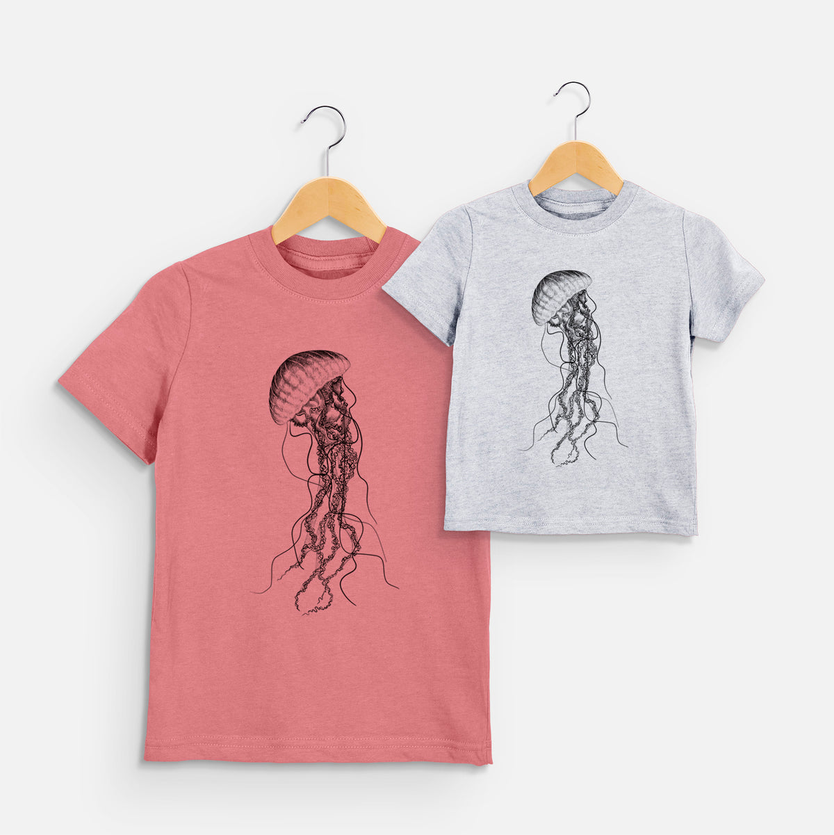 Two youth t-shirts in different colors on hangers, printed with a black ink illustration of a black sea nettle jellyfish with long trailing tentacles.