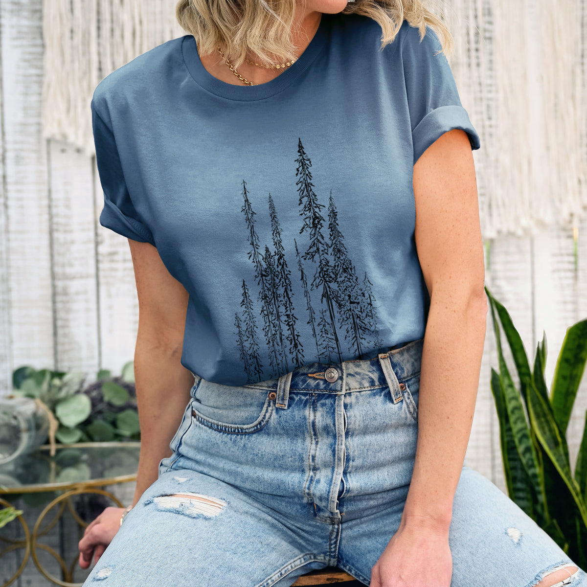 Woman wearing a steel blue lightweight cotton t-shirt printed with a black ink illustration of a stand of tall, narrow black spruce trees.