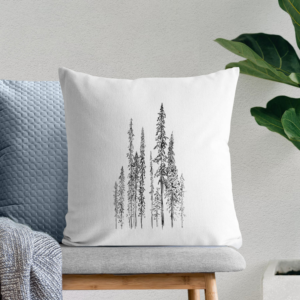 White pillow cover printed with a black ink illustration of a stand of tall, narrow black spruce trees, on a bench beside plants.