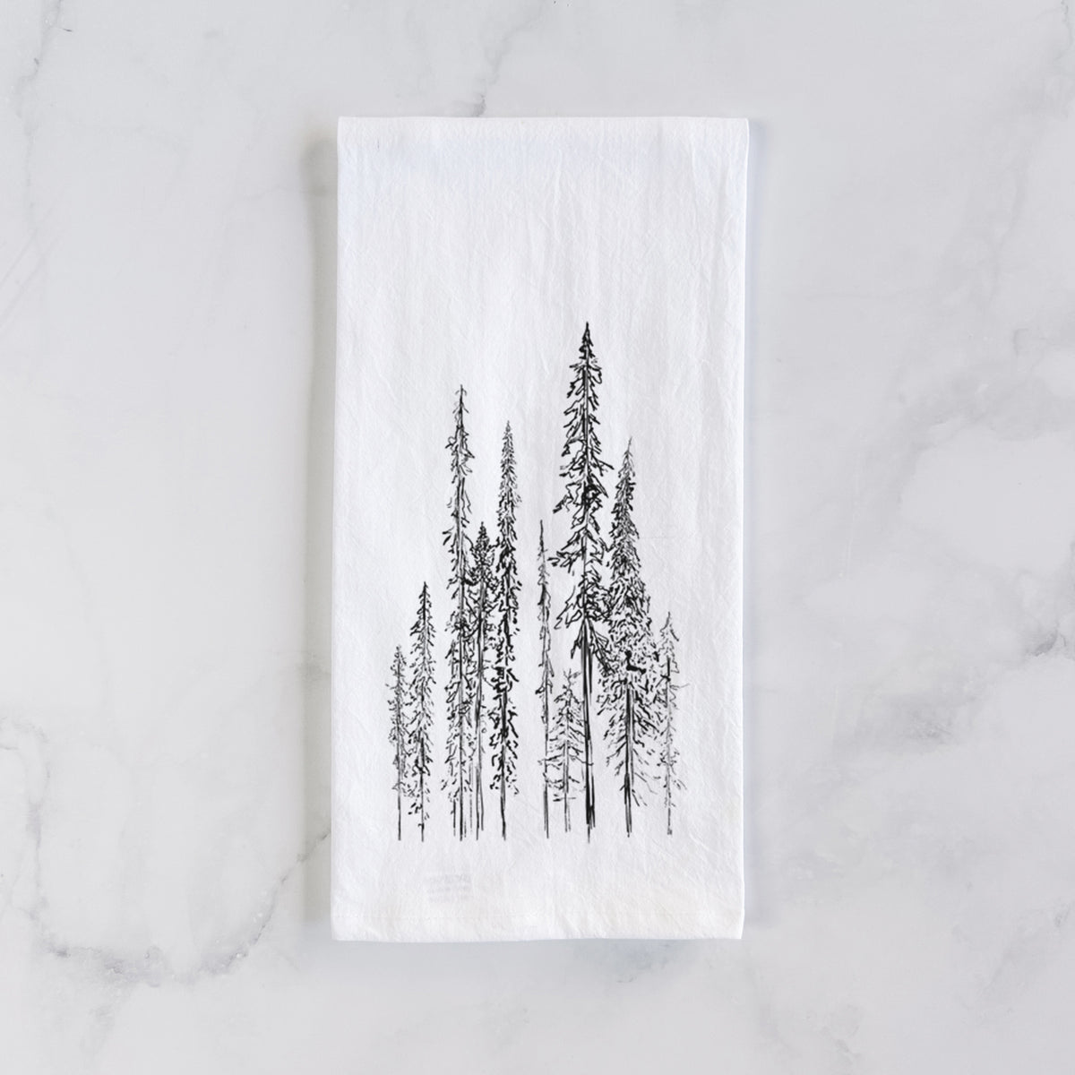 White cotton tea towel laid flat on marble, printed with a black ink illustration of a stand of tall, narrow black spruce trees.