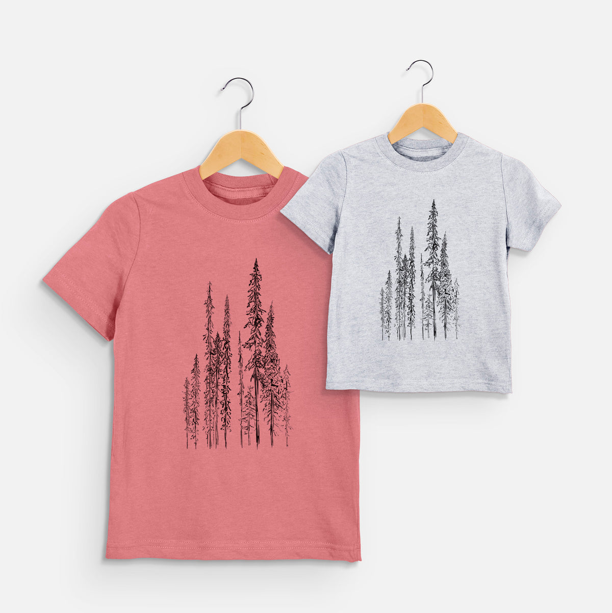 Two youth t-shirts in different colors on hangers, printed with a black ink illustration of a stand of tall, narrow black spruce trees.