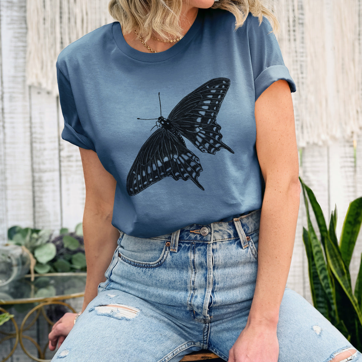 Woman wearing a steel blue lightweight cotton t-shirt printed with a detailed black ink illustration of a black swallowtail butterfly with its wings spread.