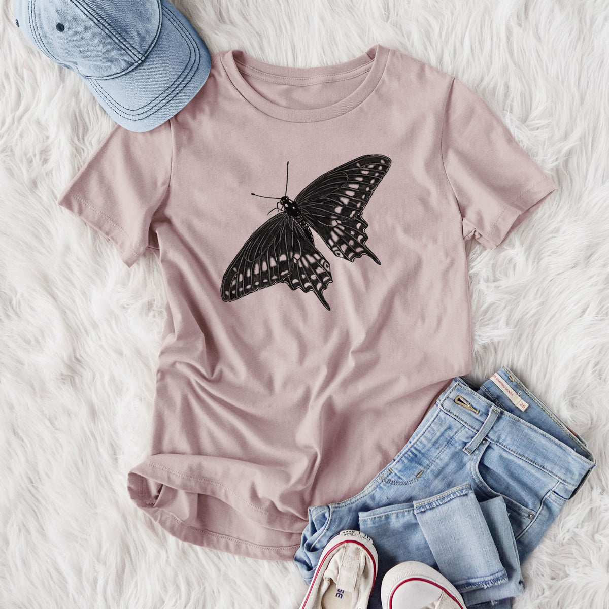 Women's relaxed fit cotton t-shirt printed with a detailed black ink illustration of a black swallowtail butterfly with its wings spread, styled flat on a white faux fur rug with jeans.