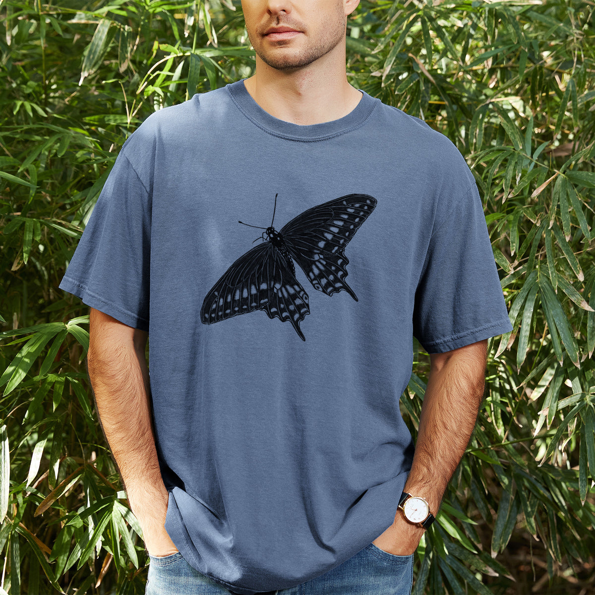 Man wearing a Comfort Colors t-shirt printed with a detailed black ink illustration of a black swallowtail butterfly with its wings spread, outdoors.