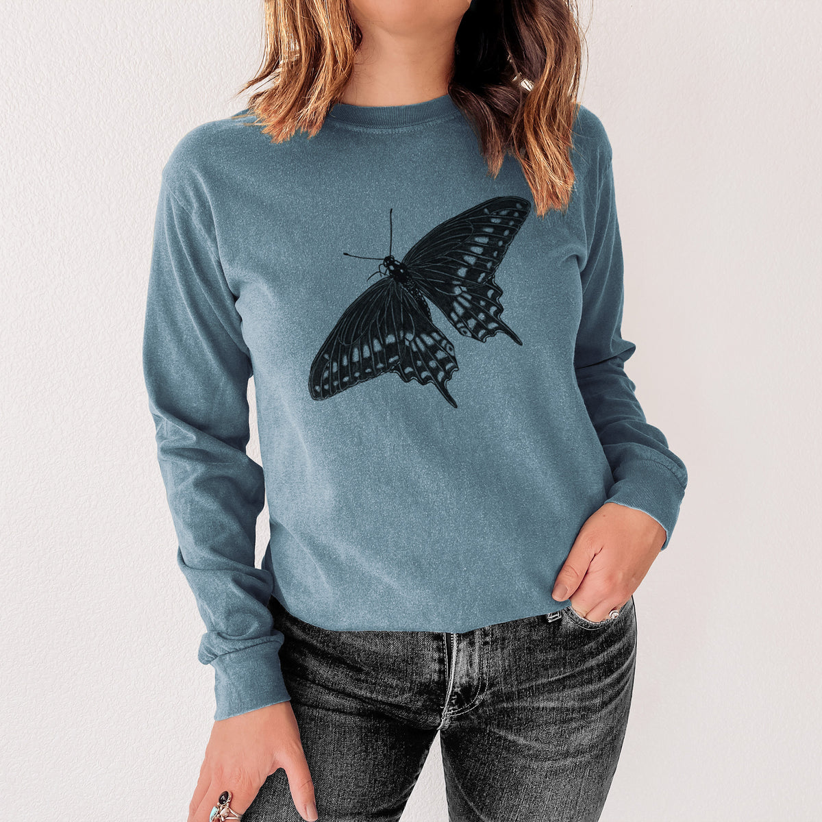 Steel blue Comfort Colors long sleeve shirt printed with a detailed black ink illustration of a black swallowtail butterfly with its wings spread, shown in a lifestyle photo.