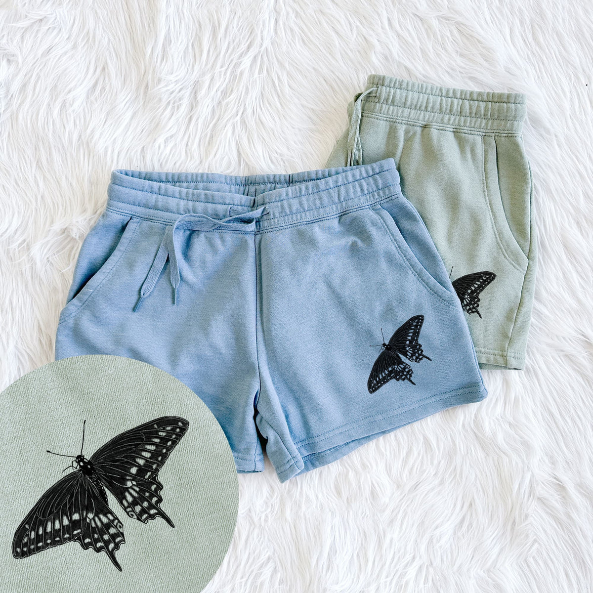 Two pairs of Cali Wave shorts in different colors printed with a detailed black ink illustration of a black swallowtail butterfly with its wings spread, with a close-up of the print.